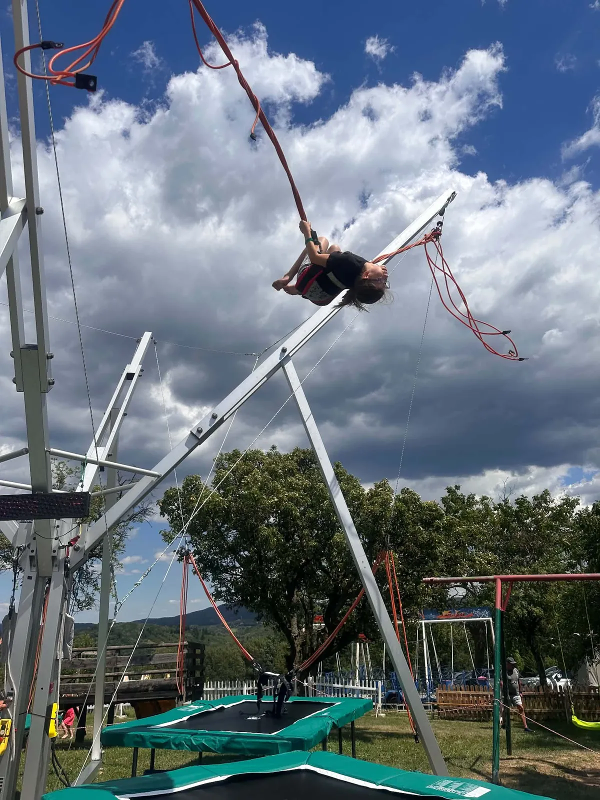 Kind dreht sich am Bungee-Trampolin hoch in der Luft, dahinter ein Wolkenhimmel
